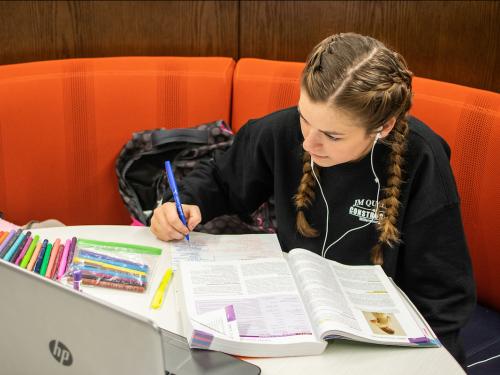 Student takes notes while reading a textbook in the library.
