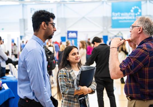 Two students interact with someone at a career expo.