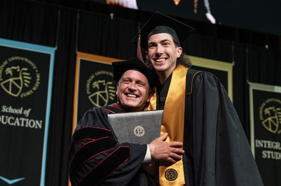 Graduating student and faculty on stage.