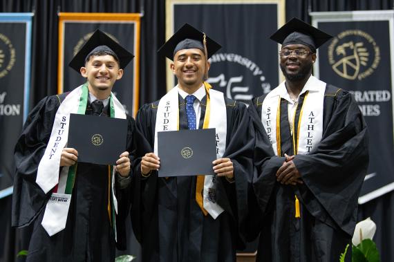 Student athletes stand on stage with diploma holders.