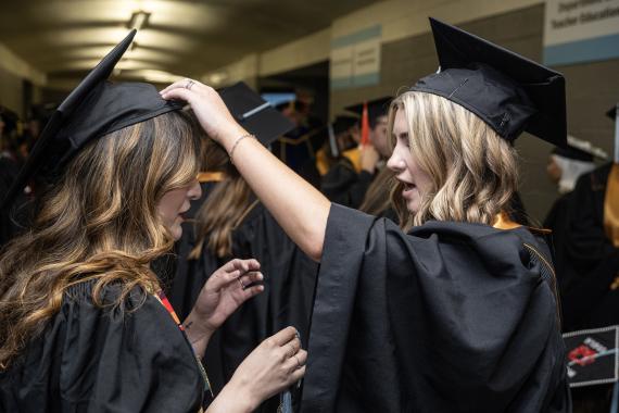 Student adjusts another’s cap.