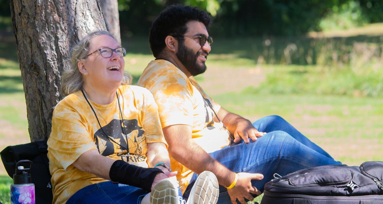 Two people are sharing a laugh while sitting under a tree.