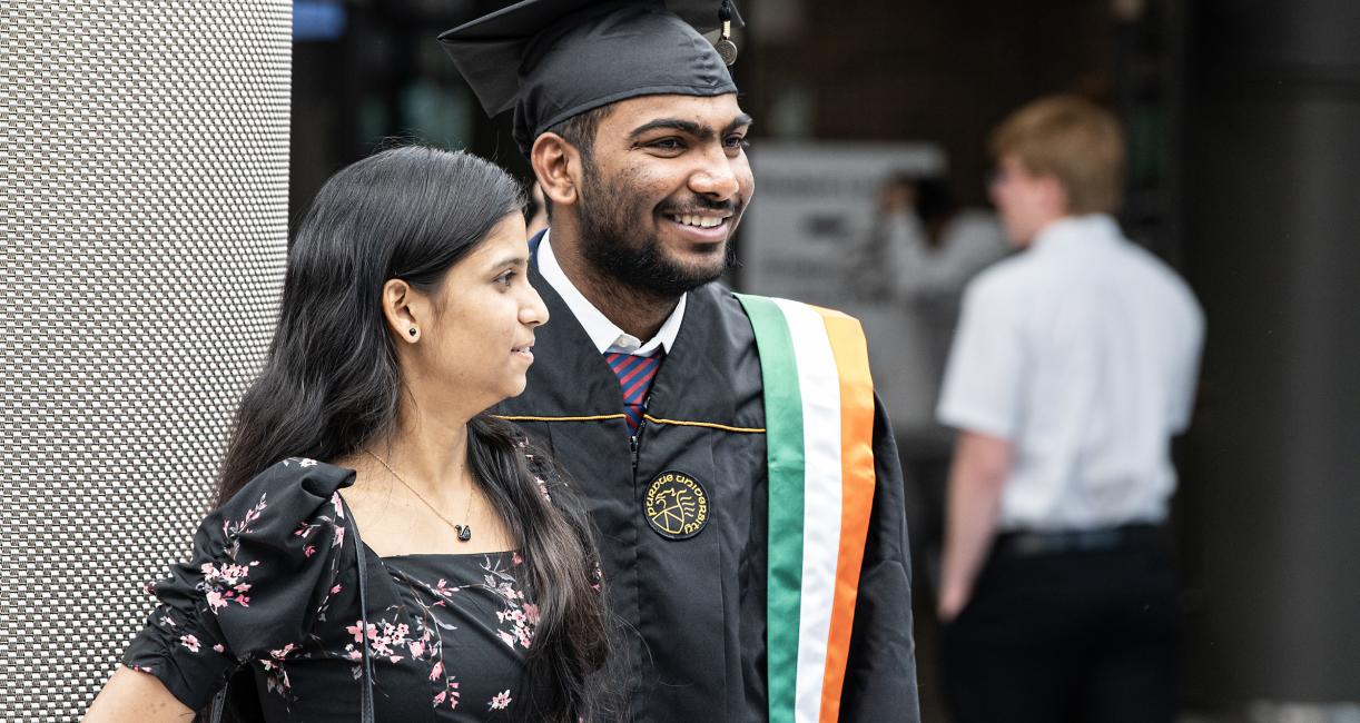 Graduating student smiles and poses with commencement guest.