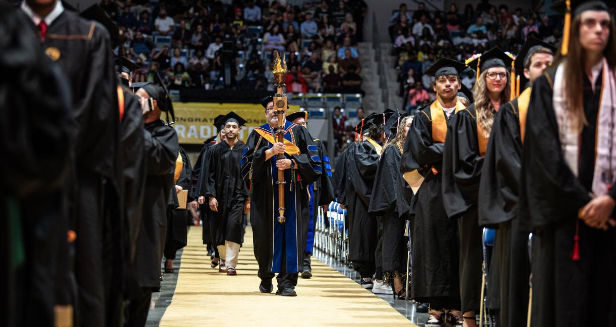 Students stand at their seats in the arena at commencement.