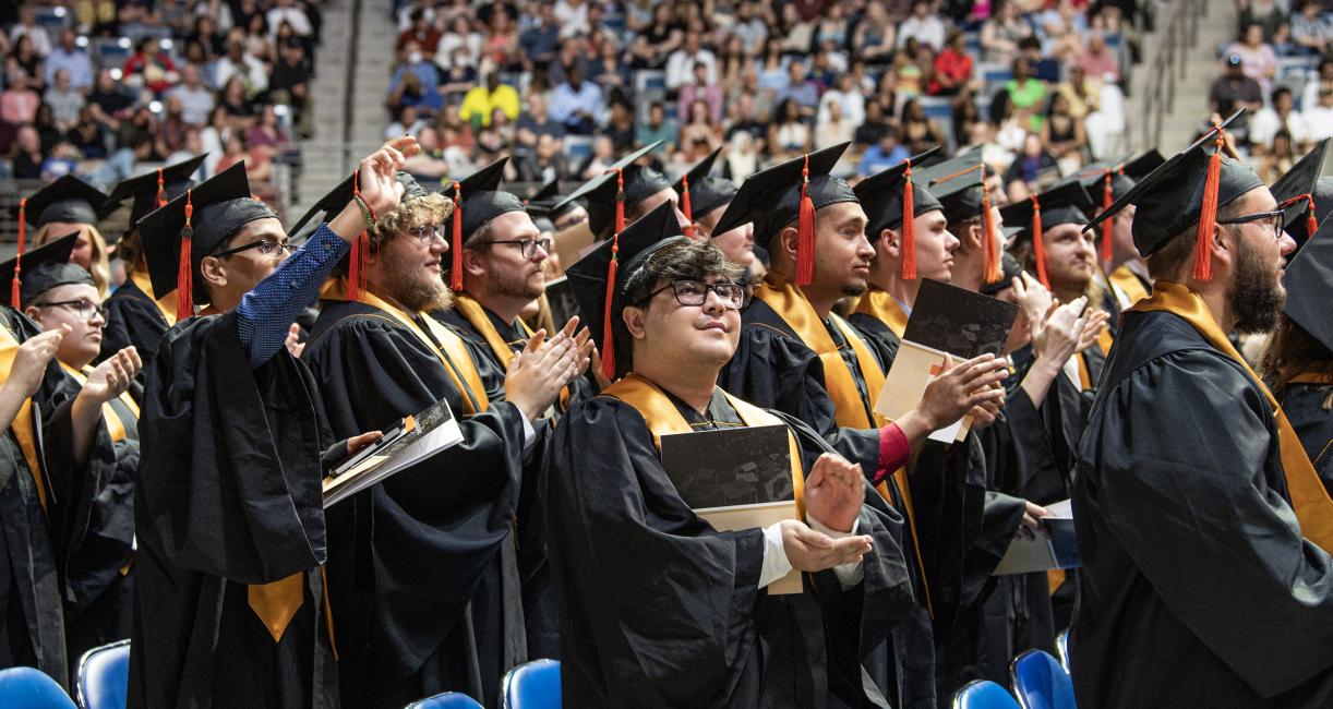 Students stand and clap at commencement.