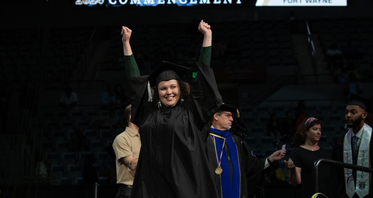 Excited graduating student raises arms in the air.