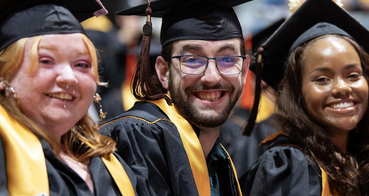 Three students in caps and gowns smile for the camera.