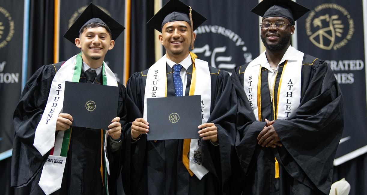 Student athletes stand on stage with diploma holders.