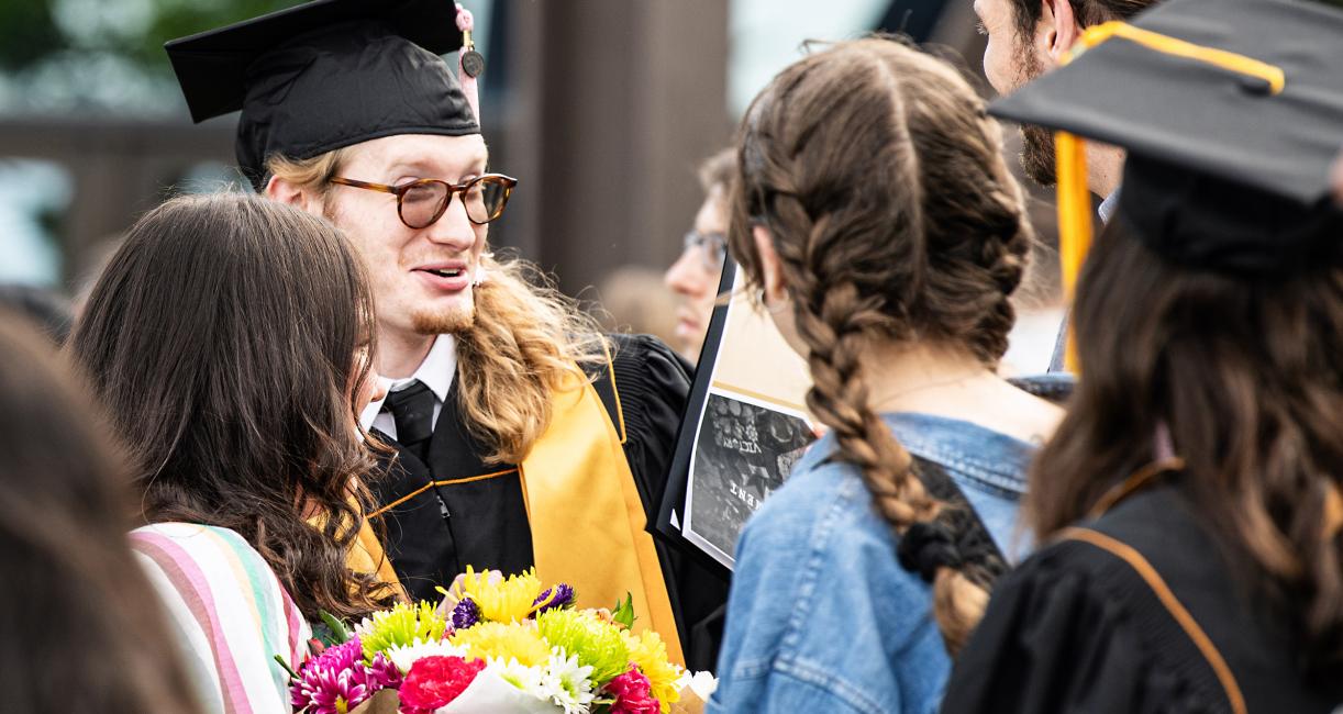 Graduates and commencement guests chat outside.