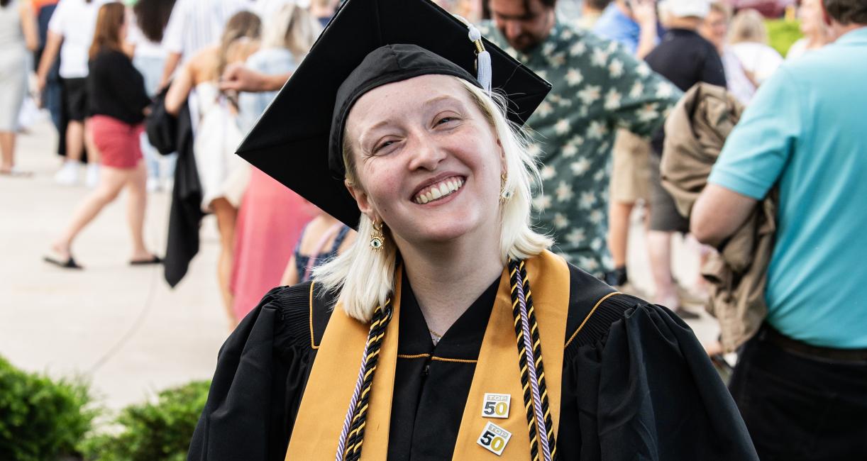 Student in cap and gown smiles at the camera.