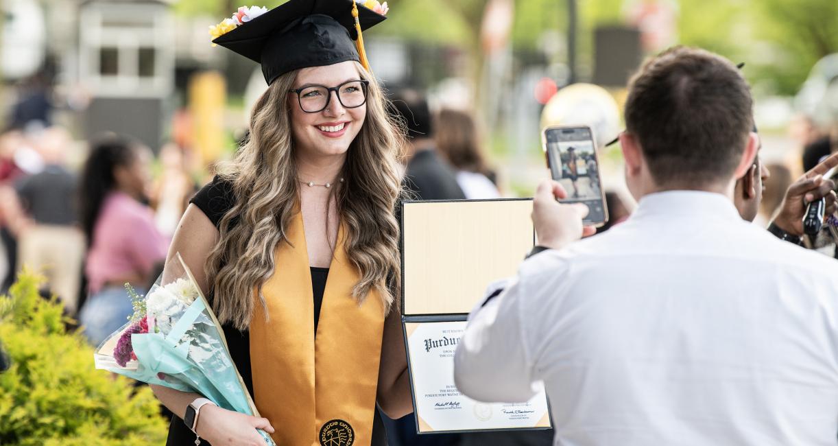 Graduated student poses with flowers and degree holder.