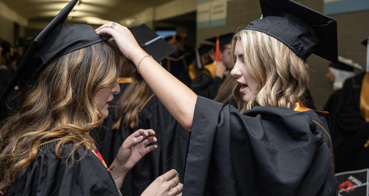 Student adjusts another’s cap.