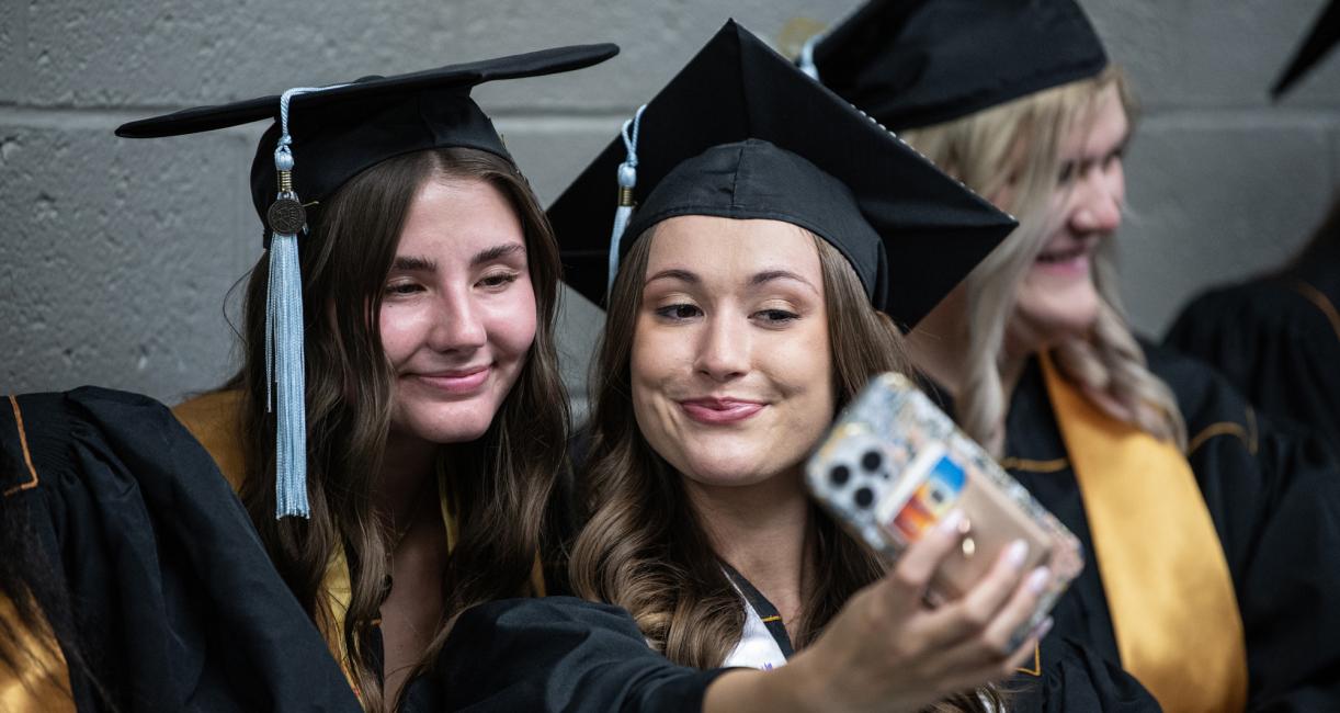 Students in caps and gowns take a selfie.